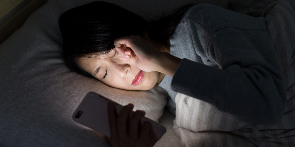 Mulher esfregando os olhos enquanto usa o telefone à noite
